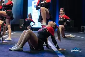 Athlètes de cheerleading réalisant une chorégraphie au championnat régional, avec une athlète en position assise sur scène.